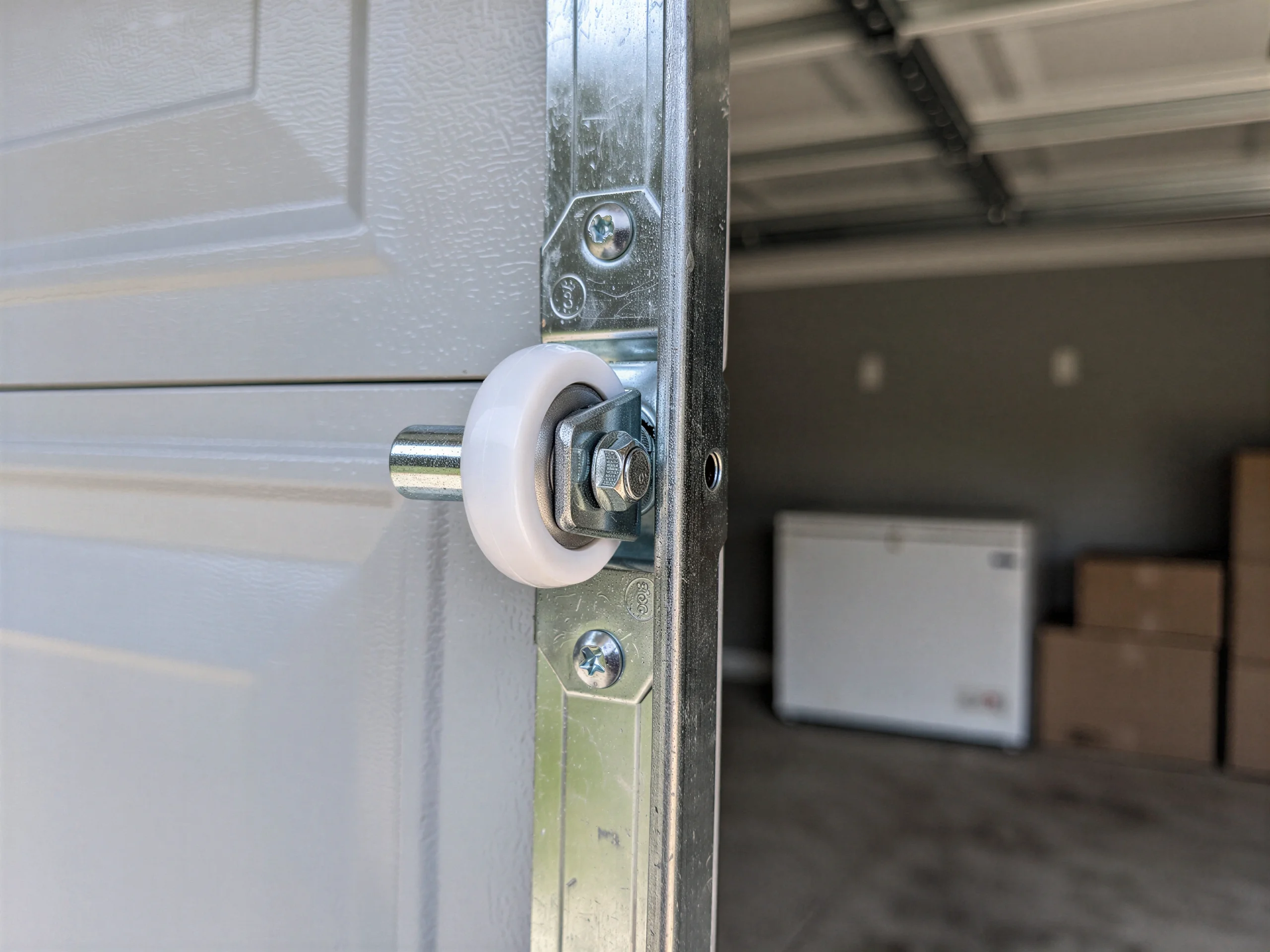A white garage door roller is attached to a metal track.